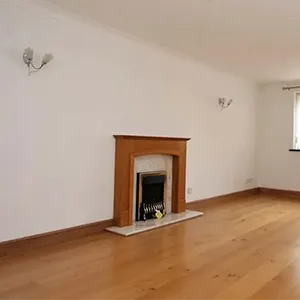 An empty living room with a fireplace and hard wood floors.